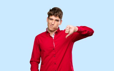 Yakışıklı genç adam, izole edilmiş mavi arkaplanda baş parmak izi gösteriyor.