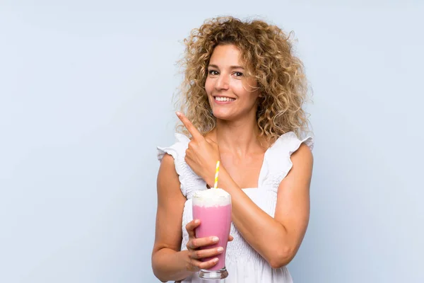 Young Blonde Woman Curly Hair Holding Strawberry Milkshake Pointing Side — 스톡 사진