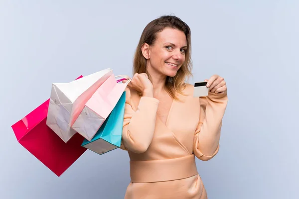 Blonde Frau Über Isoliertem Blauem Hintergrund Mit Einkaufstaschen Und Kreditkarte — Stockfoto