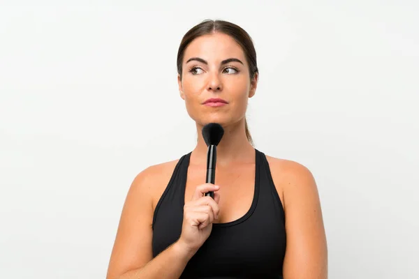 Jonge vrouw over geïsoleerde witte achtergrond met make-up borstel — Stockfoto