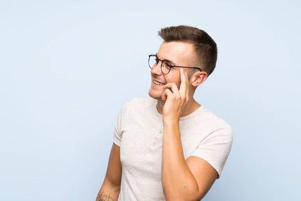 Mladý Pohledný Blonďatý Muž Přes Izolované Modré Pozadí Brýlemi — Stock fotografie