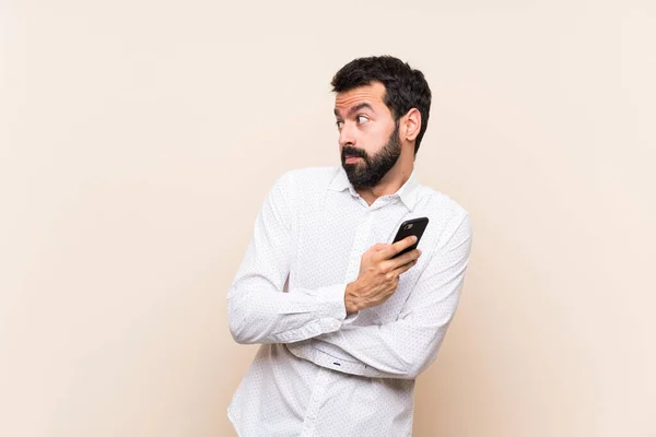 Joven Con Barba Sosteniendo Móvil Haciendo Gestos Dudas Mientras Levanta —  Fotos de Stock