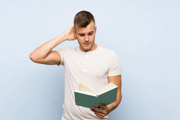 Joven Guapo Hombre Rubio Sobre Fondo Azul Aislado Sosteniendo Leyendo —  Fotos de Stock