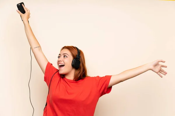 Adolescente rousse fille écoute de la musique avec un mobile sur fond isolé — Photo