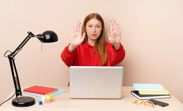 Young student woman in a workplace with a laptop making stop gesture and disappointed