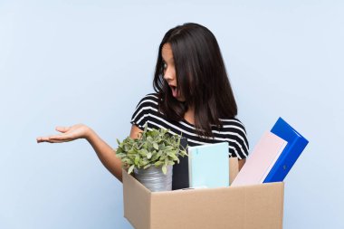 Young brunette girl making a move while picking up a box full of things with surprise facial expression