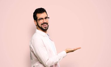 Handsome man with beard presenting an idea while looking smiling towards over isolated pink background