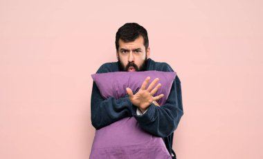 Man with beard in pajamas nervous stretching hands to the front over isolated pink background
