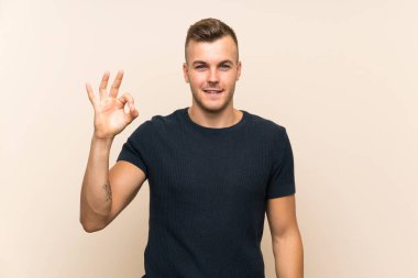 Genç yakışıklı sarışın adam izole edilmiş arka planda parmaklarıyla işaret veriyor.