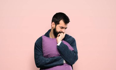 Man with beard in pajamas having doubts over isolated pink background