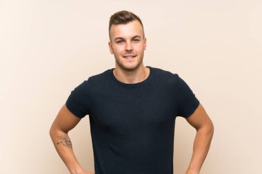 Sarışın, genç, soyutlanmış, kalçasında kollarıyla poz veren ve gülümseyen bir adam.