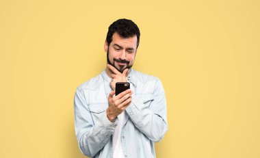 Handsome man with beard thinking and sending a message over isolated yellow background