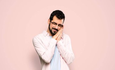 Handsome man with beard making sleep gesture in dorable expression over isolated pink background