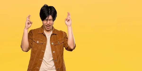 Asian Man Brown Jacket Fingers Crossing Isolated Yellow Background — 스톡 사진