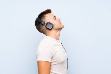Izole mavi arka plan üzerinde genç yakışıklı sarışın adam kulaklık ile müzik dinlerken