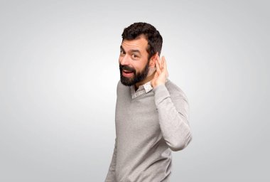 Handsome man listening to something by putting hand on the ear over isolated grey background
