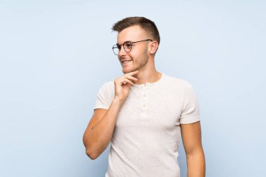 Gözlüklü izole mavi arka plan üzerinde genç yakışıklı sarışın adam