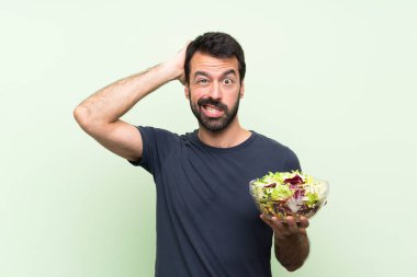 Yeşil duvarın üstünde salatalı yakışıklı genç adam hayal kırıklığına uğradı ve ellerini başının üstüne koydu.