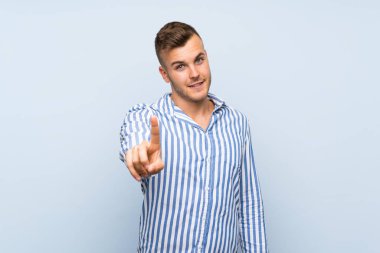 Genç, sarışın, soyutlanmış, mavi arka planda bir parmağını kaldırıp kaldıran adam.