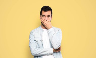 Handsome man with beard covering mouth with hands over isolated yellow background