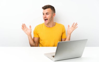Sürpriz yüz ifadesi ile bir dizüstü bilgisayar ile bir masada genç sarışın adam