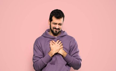 Handsome man with sweatshirt having a pain in the heart over isolated pink background