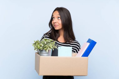 Young brunette girl making a move while picking up a box full of things looking up while smiling