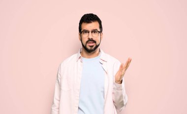 Handsome man with beard making doubts gesture over isolated pink background