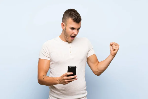 Joven Guapo Hombre Rubio Sobre Fondo Azul Aislado Usando Teléfono —  Fotos de Stock