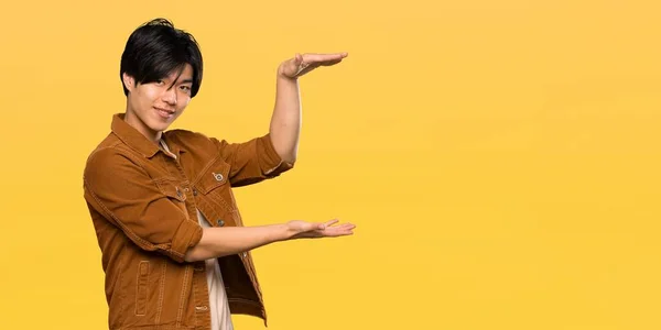 Asian Man Brown Jacket Holding Copyspace Insert Isolated Yellow Background — 스톡 사진