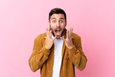 Sakallı genç yakışıklı bir adam pembe arka planda kadife ceket giyiyor ve yüzünde sürpriz bir ifade var.