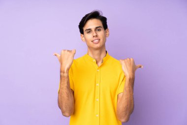 İzole edilmiş mor arka planı olan bir adam. Baş parmakları havada ve gülümsüyor.
