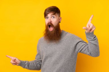 Sarı arka planda uzun sakallı kızıl saçlı adam parmak uçlarını işaret ediyor ve mutlu.