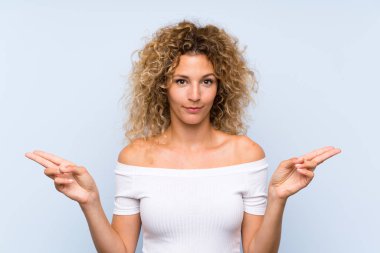 Kıvırcık saçlı, soyutlanmış mavi arka planı olan genç sarışın kadın, yan taraftaki kuşkuları gösteriyor.