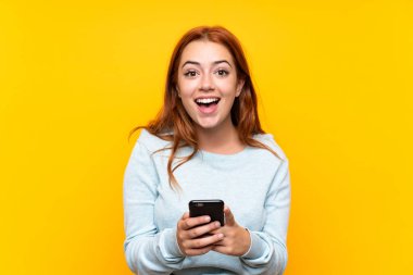 Izole sarı arka plan üzerinde Genç redhead kız şaşırttı ve bir mesaj gönderme