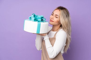 Genç pasta şefi mor arka planda büyük bir pasta tutuyor.