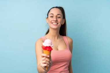 Kornet dondurmalı genç esmer kadın izole edilmiş mavi arka planda mutlu bir ifadeyle.