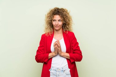 Sarışın, kıvırcık saçlı, izole edilmiş yeşil arka planı olan genç bir kadın bir şeyler planlıyor.