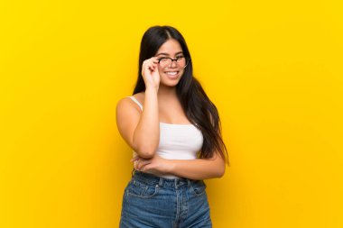 Young teenager Asian girl over isolated yellow background with glasses and happy