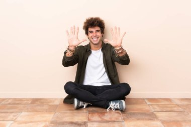 Beyaz bir adam yerde oturmuş parmaklarıyla 10 'a kadar sayıyor.