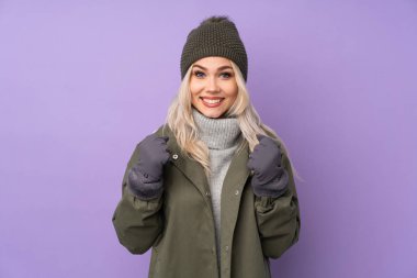 Kışlık şapkalı, mor arka planda genç sarışın kız galibiyeti kutluyor.