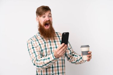 Kızıl saçlı, uzun sakallı, izole edilmiş beyaz arka planı olan, elinde kahve ve cep telefonu olan bir adam.