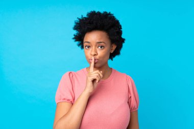İzole edilmiş mavi arka plan üzerinde sessiz jest yapan Afrikalı Amerikalı bir kadın.