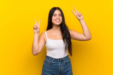 Young teenager Asian girl over isolated yellow background showing victory sign with both hands