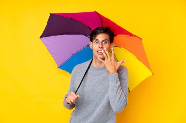 Sarı arka planda şemsiye tutan adamın yüzünde sürpriz bir ifade var.