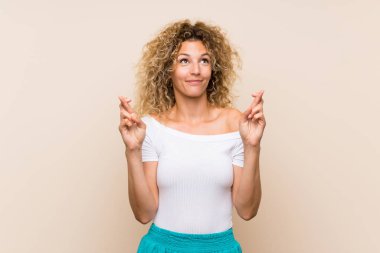 Parmakları geçiş ve en iyi dilek ile izole arka plan üzerinde kıvırcık saçlı genç sarışın kadın