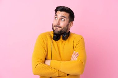 Kulaklıklı, pembe arka planda genç, yakışıklı bir adam omuzlarını kaldırırken şüpheyle hareket ediyor.