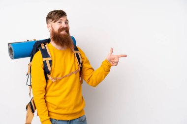 İzole edilmiş beyaz arka plan üzerinde büyük bir sırt çantası olan dağcı genç adam parmağını yana doğru gösteriyor.
