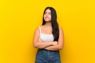 Young teenager Asian girl over isolated yellow background with confuse face expression