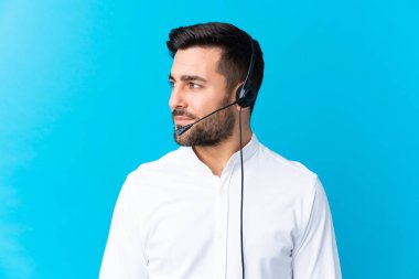 Tele pazarlamacı, mavi arka plan üzerinde çalışan bir kulaklıkla yan tarafa bakıyor